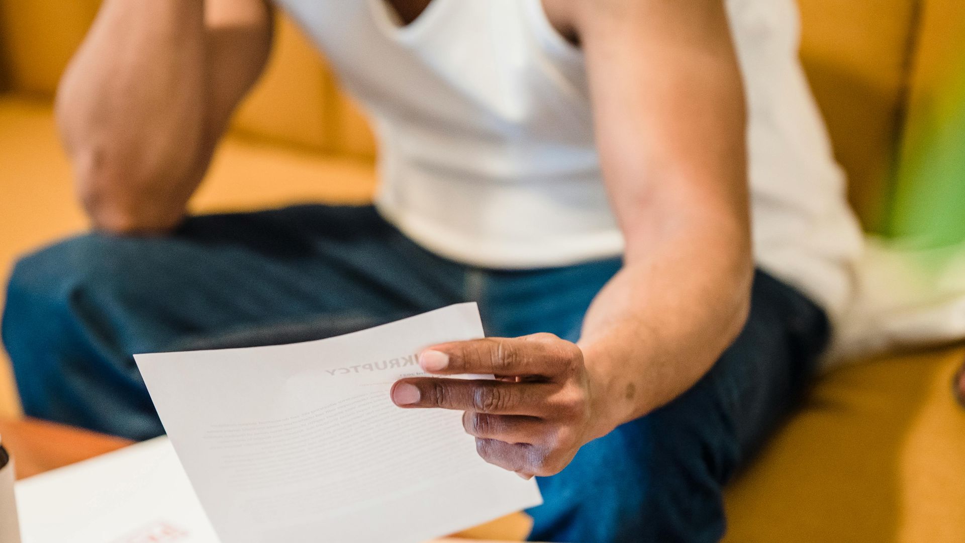 Man sitting on sofa reading unpaid bills, looking stressed and concerned over financial debt.