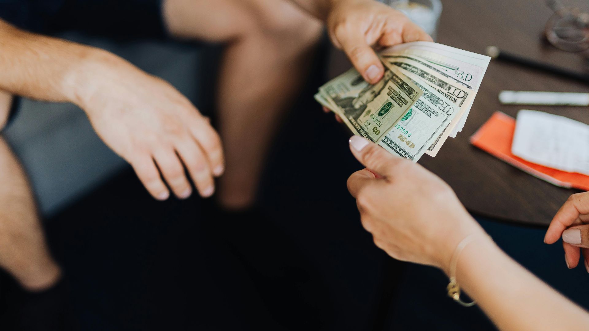 Close-up of hands exchanging US dollar bills, symbolizing a financial transaction or payment.