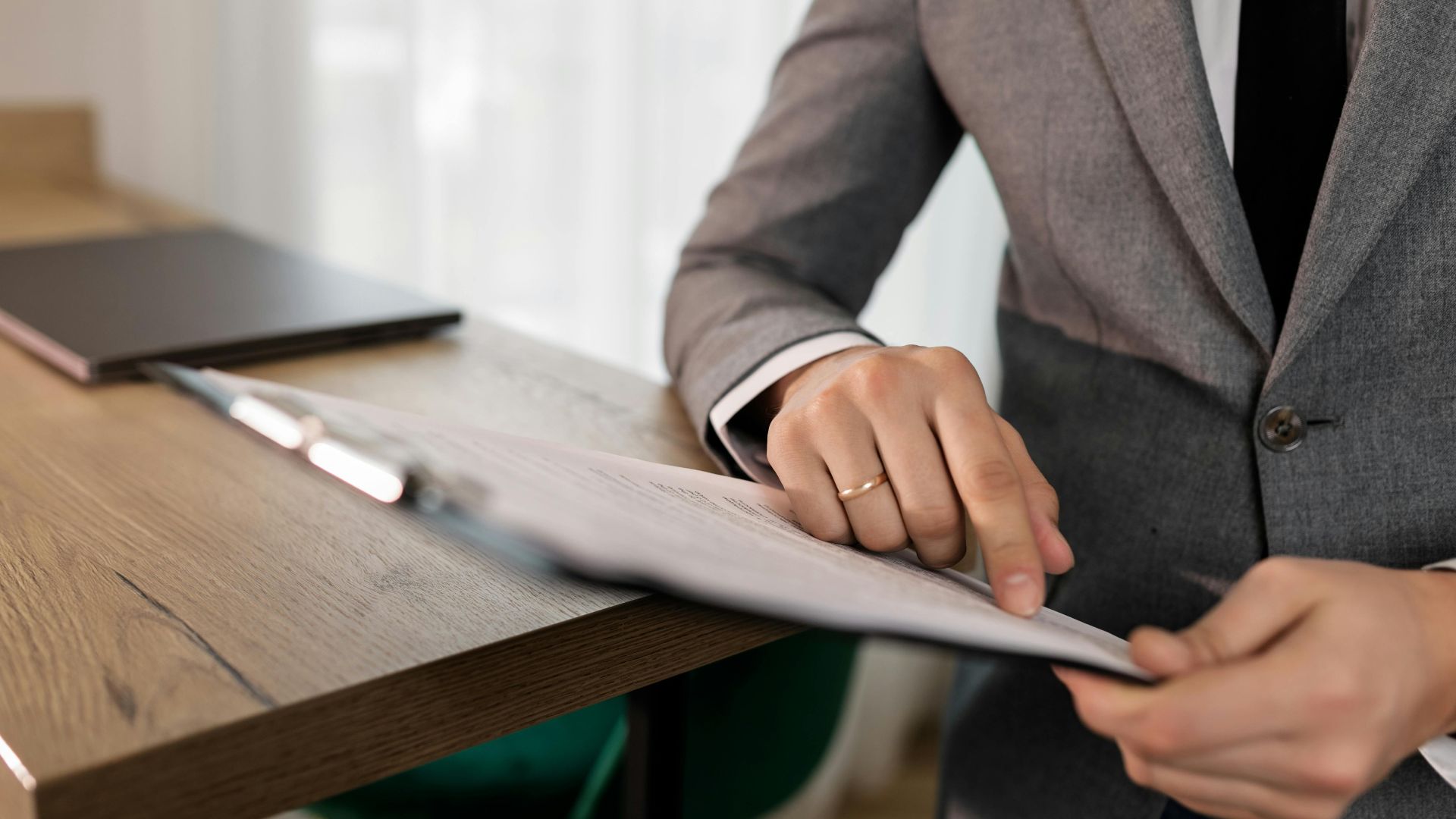Professional businessman in suit reviewing documents on clipboard at office desk.