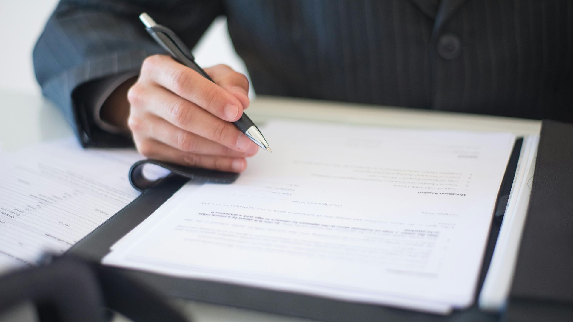 Close-up of a hand signing documents with a pen, symbolizing an important business contract.