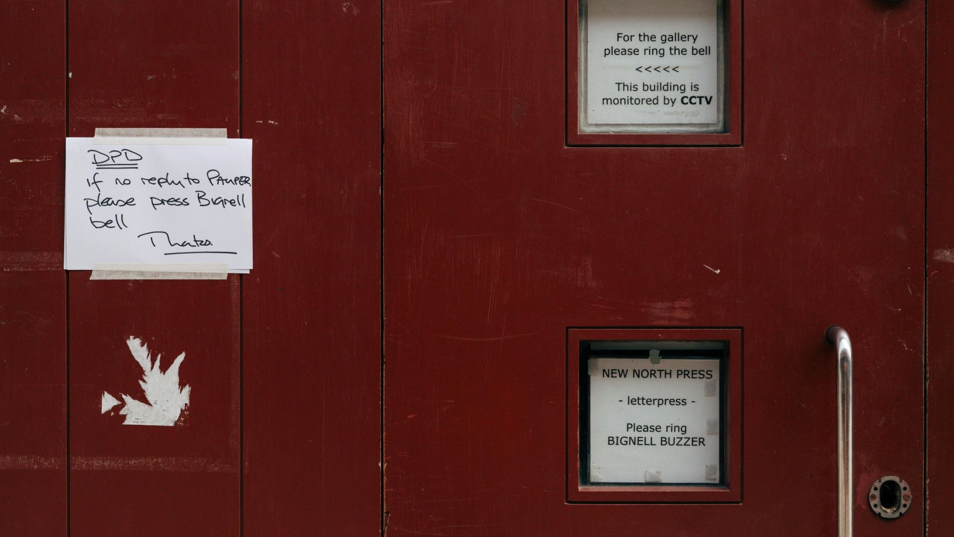 Red door with small windows and posted notices outdoors.