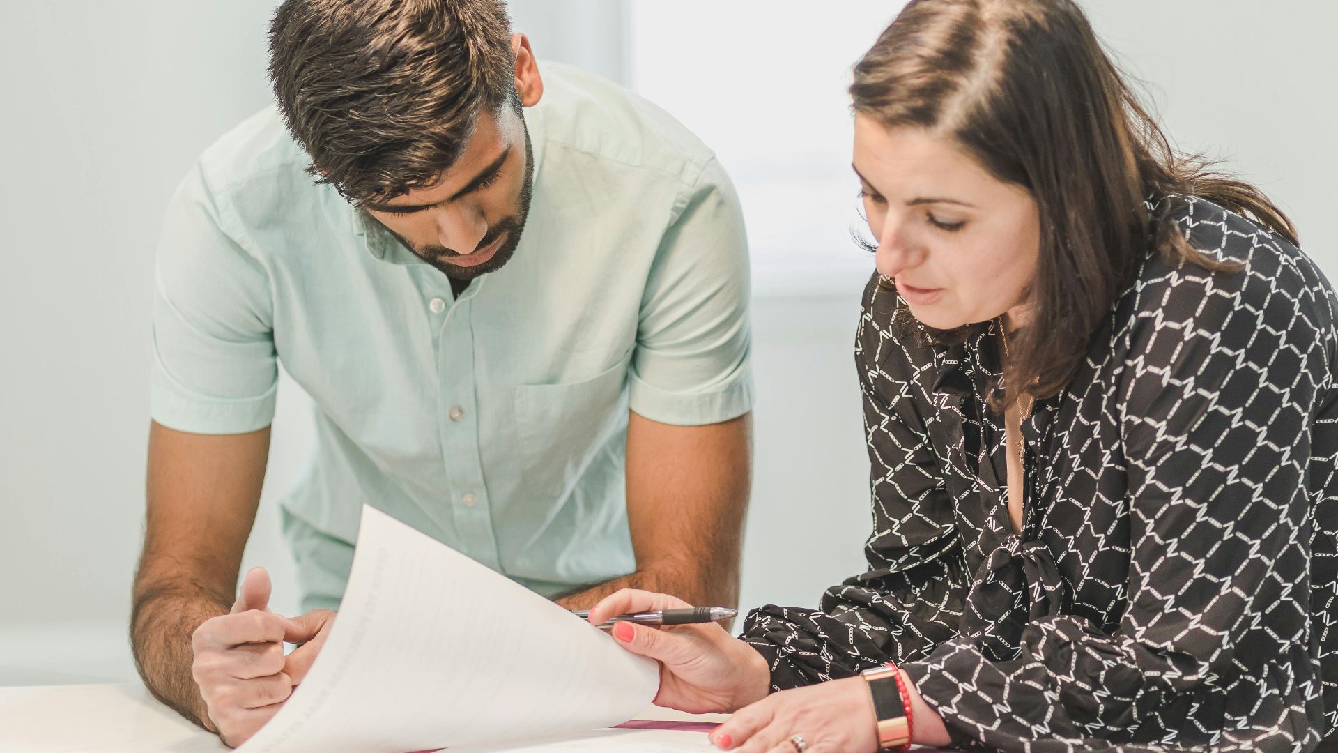 Real estate agent assisting first-time homebuyer with documents inside a bright room.