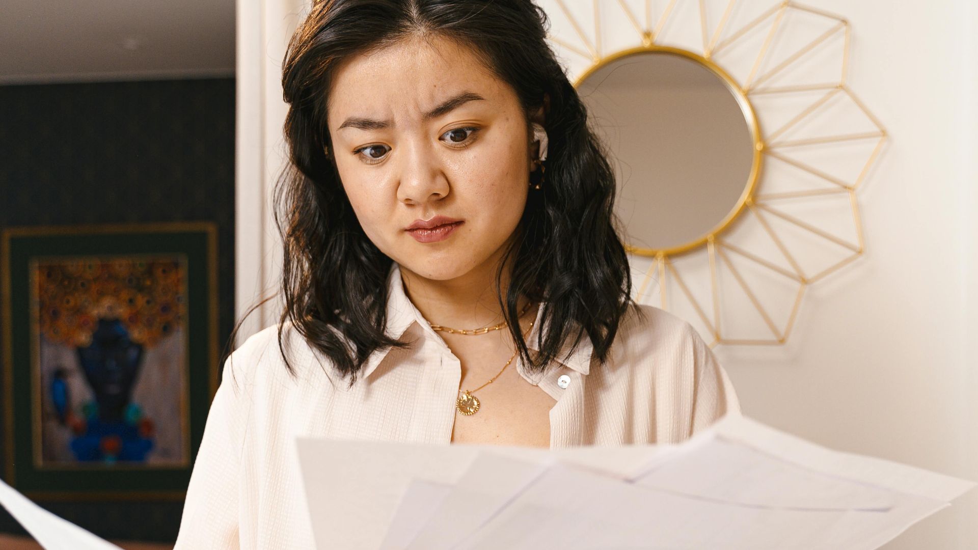 Young woman looks confused while reviewing documents in a modern home interior.