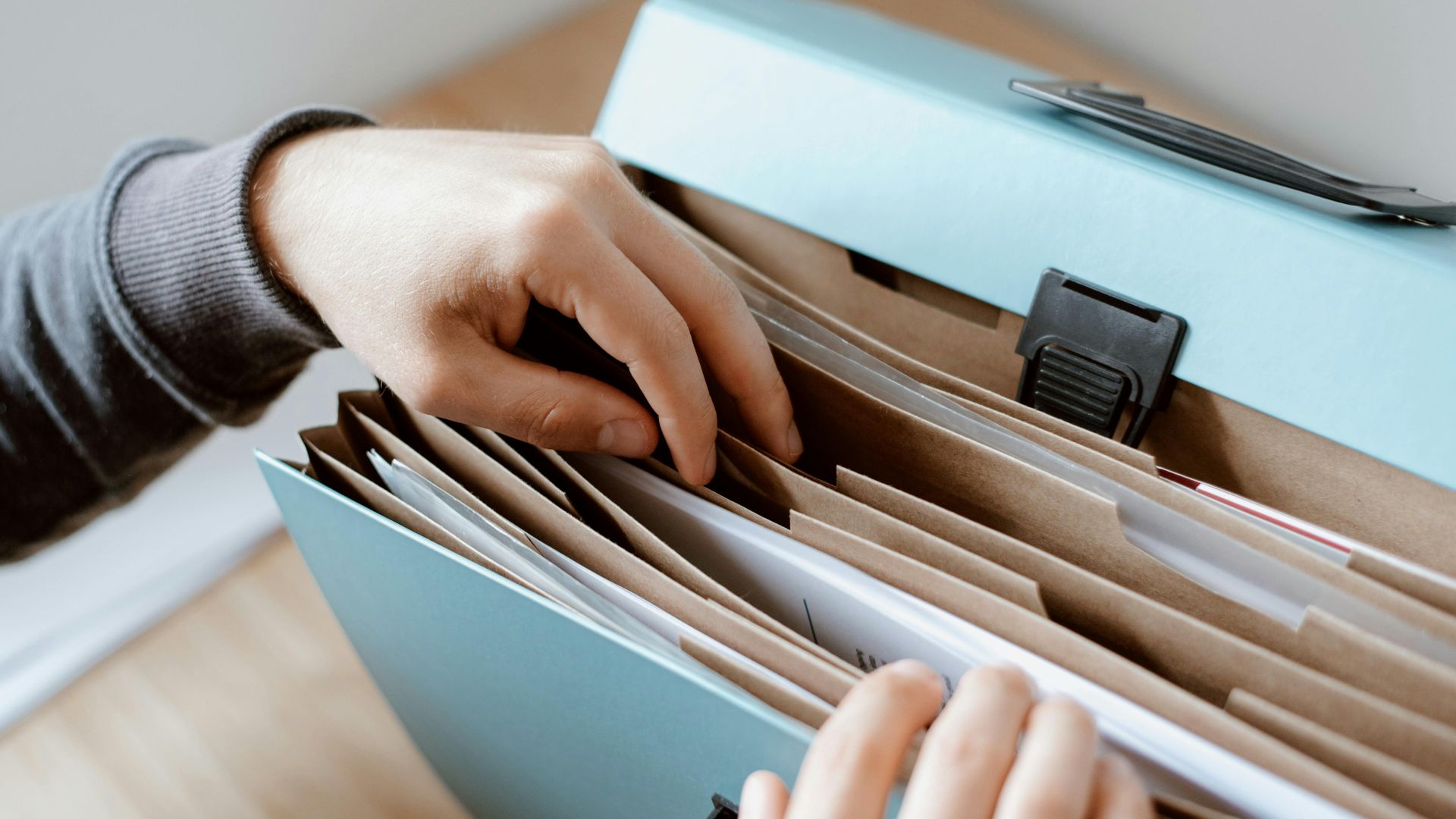 Crop unrecognizable person selecting document in opened briefcase for documents placed on wooden table