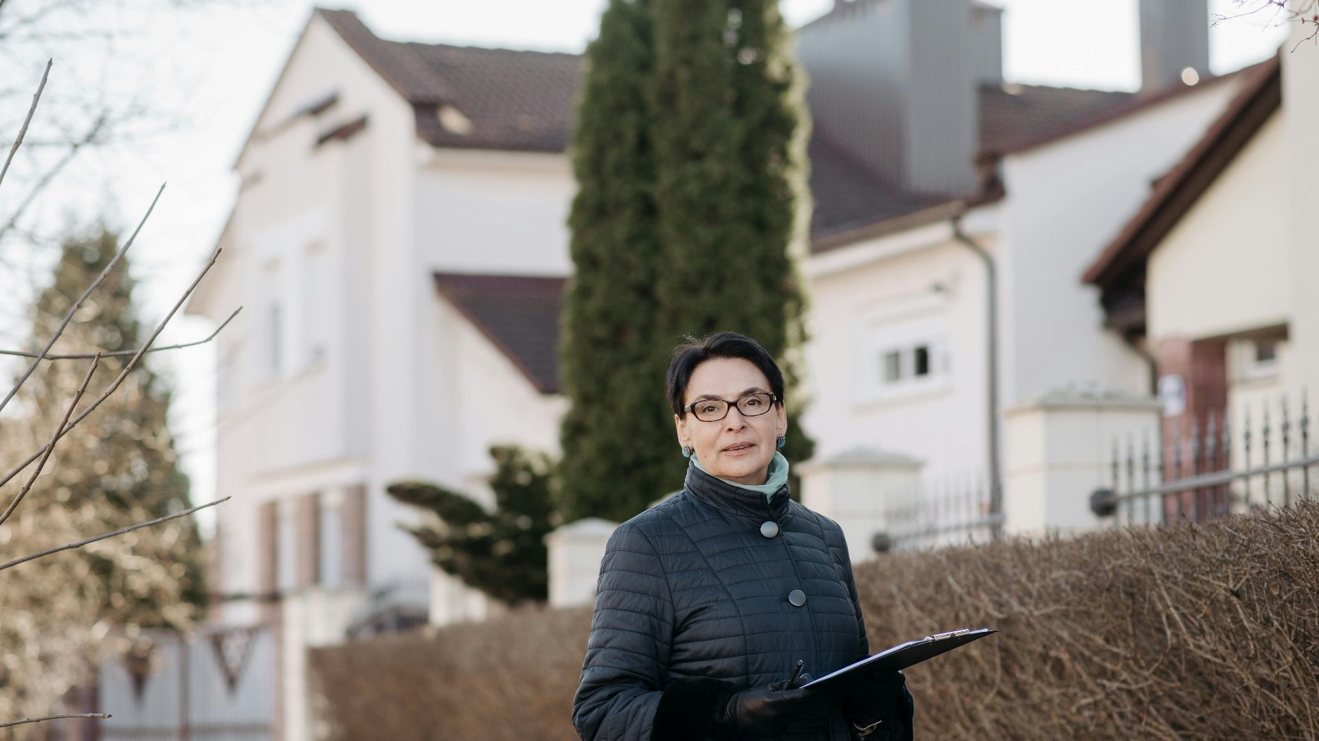 Adult woman in eyeglasses standing outside holding a clipboard, ideal for business or lifestyle themes.