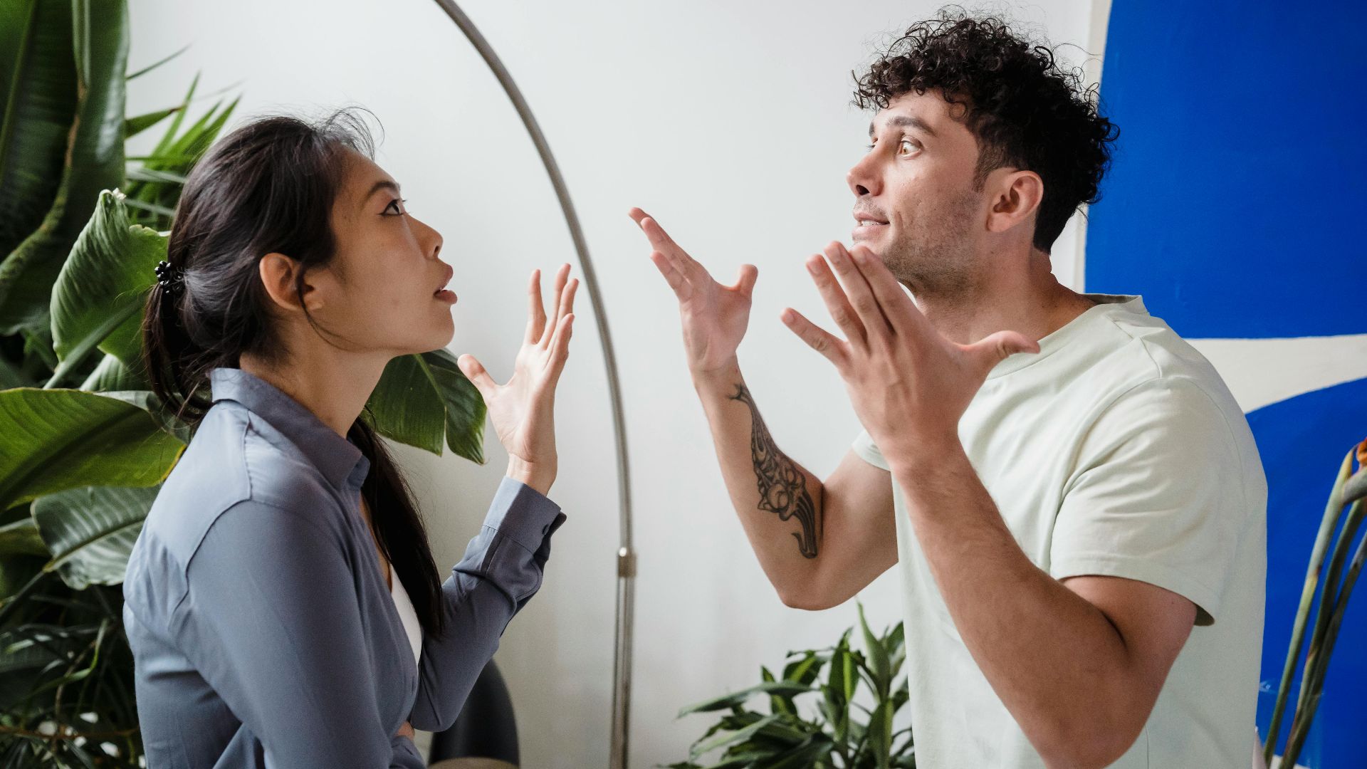 A couple argues indoors amidst greenery, showcasing emotions and interpersonal conflict.