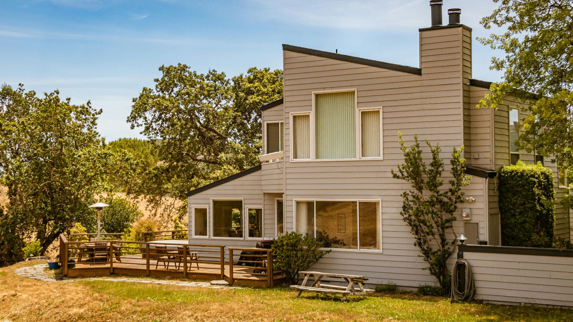 Contemporary suburban house featuring large glass windows and a spacious deck in a lush outdoor setting.