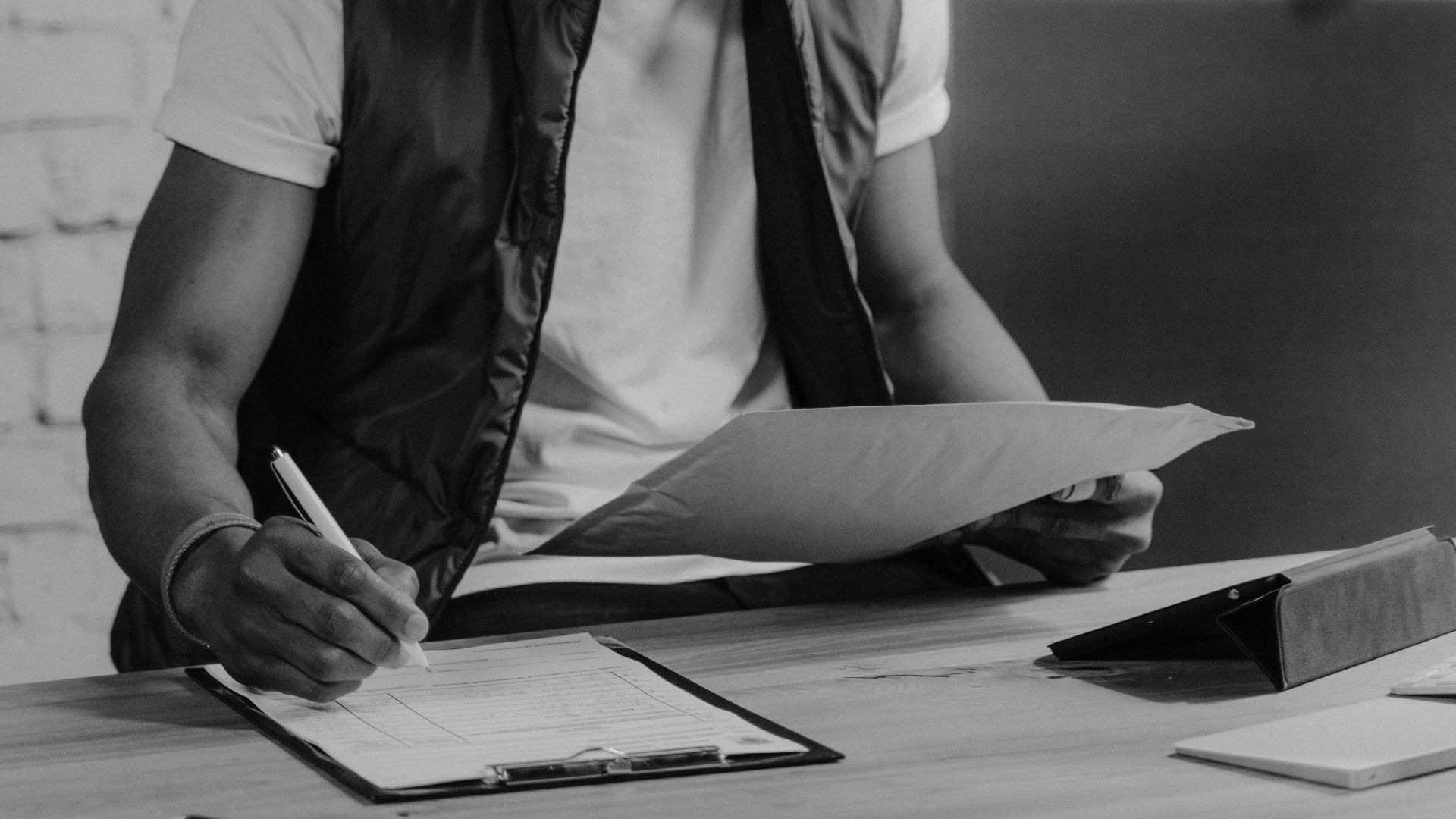 Monochrome photograph of a man writing at a desk, focusing on tasks.
