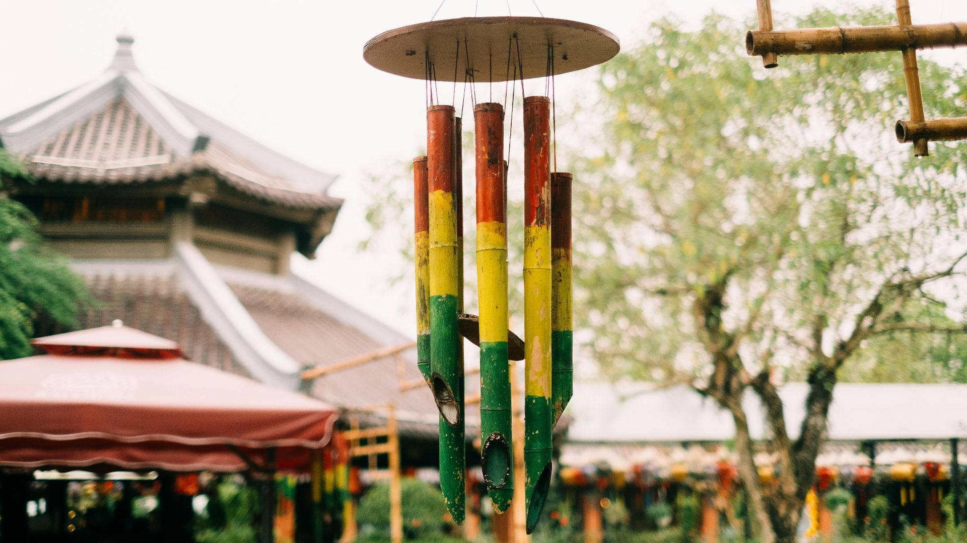 Vibrant bamboo wind chimes hanging in a tranquil Asian garden setting with a traditional building backdrop.