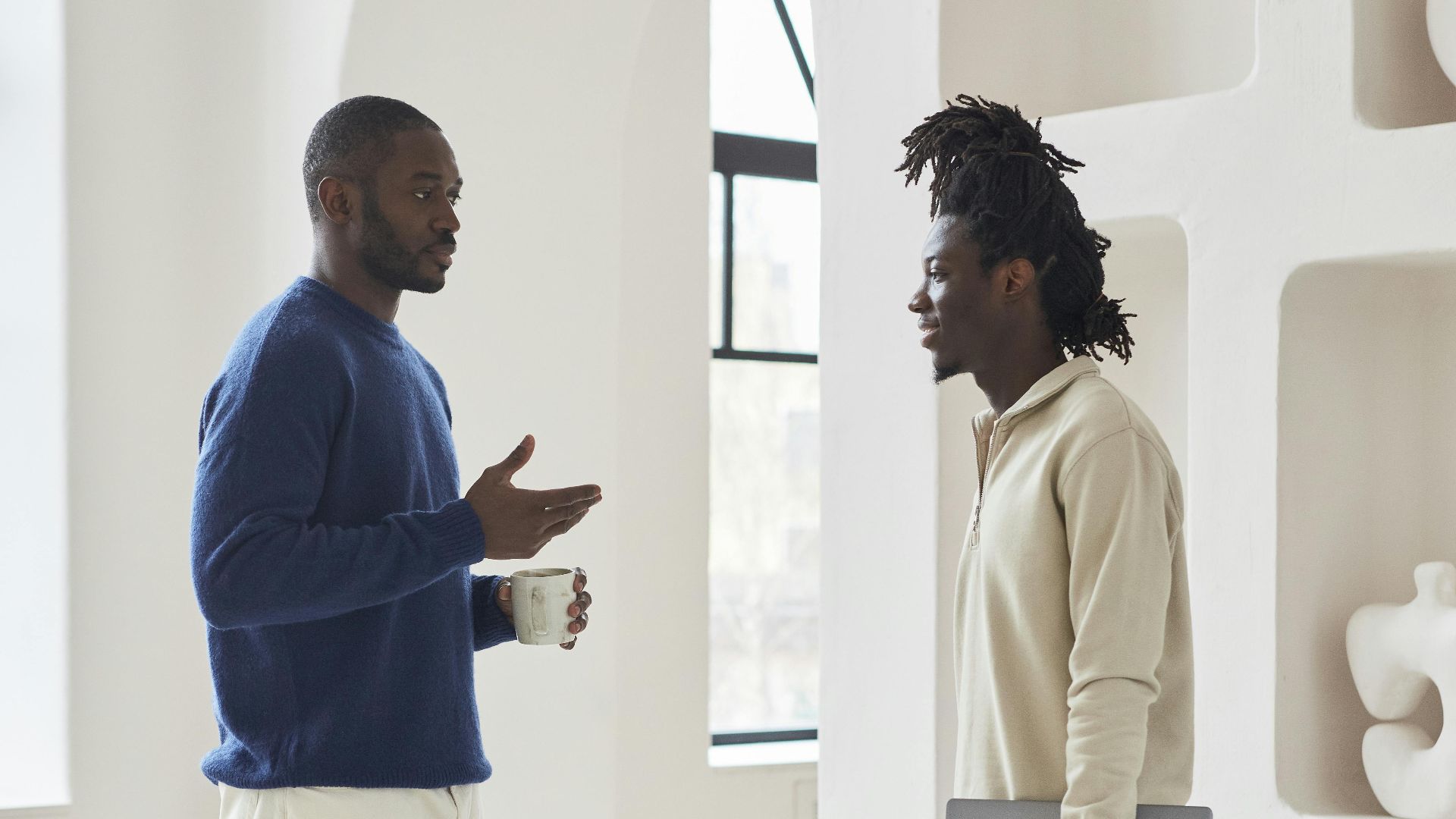 Two men conversing in a modern indoor setting, discussing work and ideas.