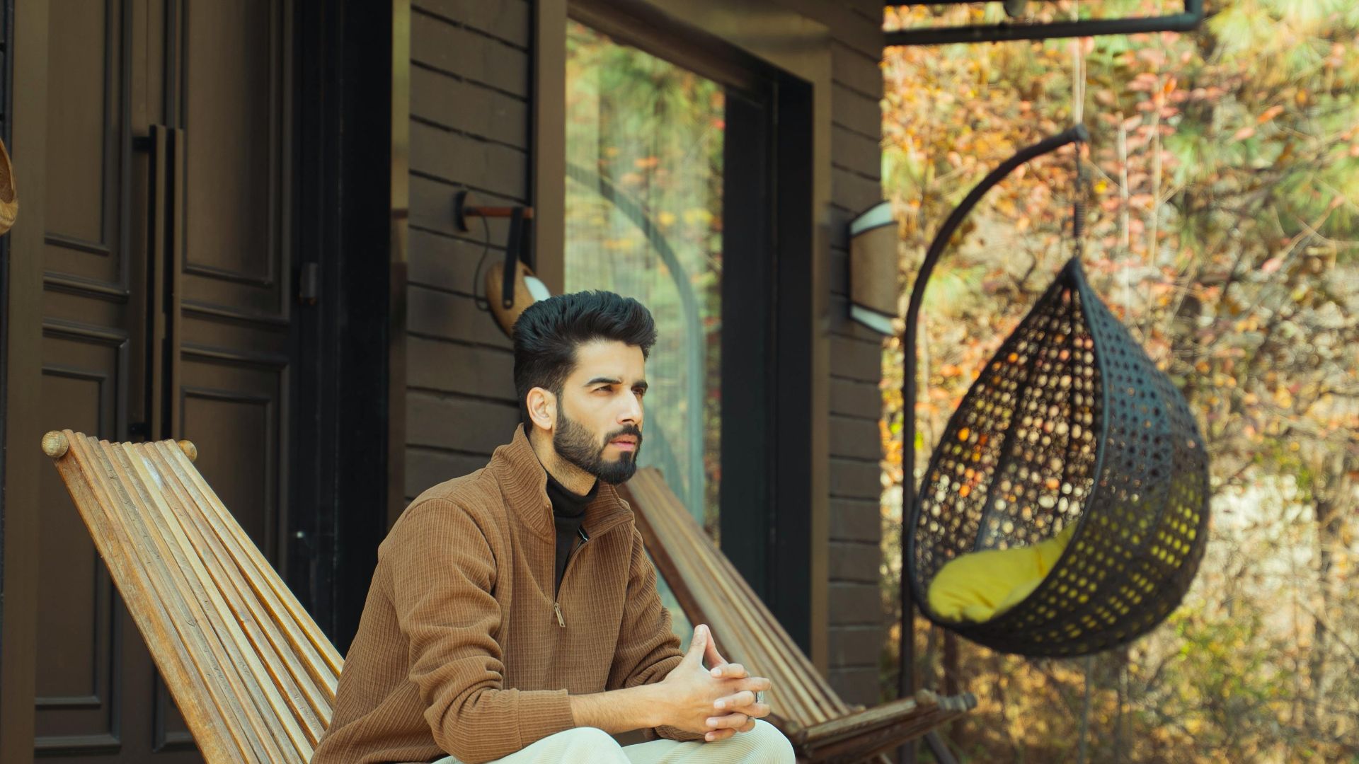 A man sits on a deck chair outside a modern wooden cabin on a sunny day.