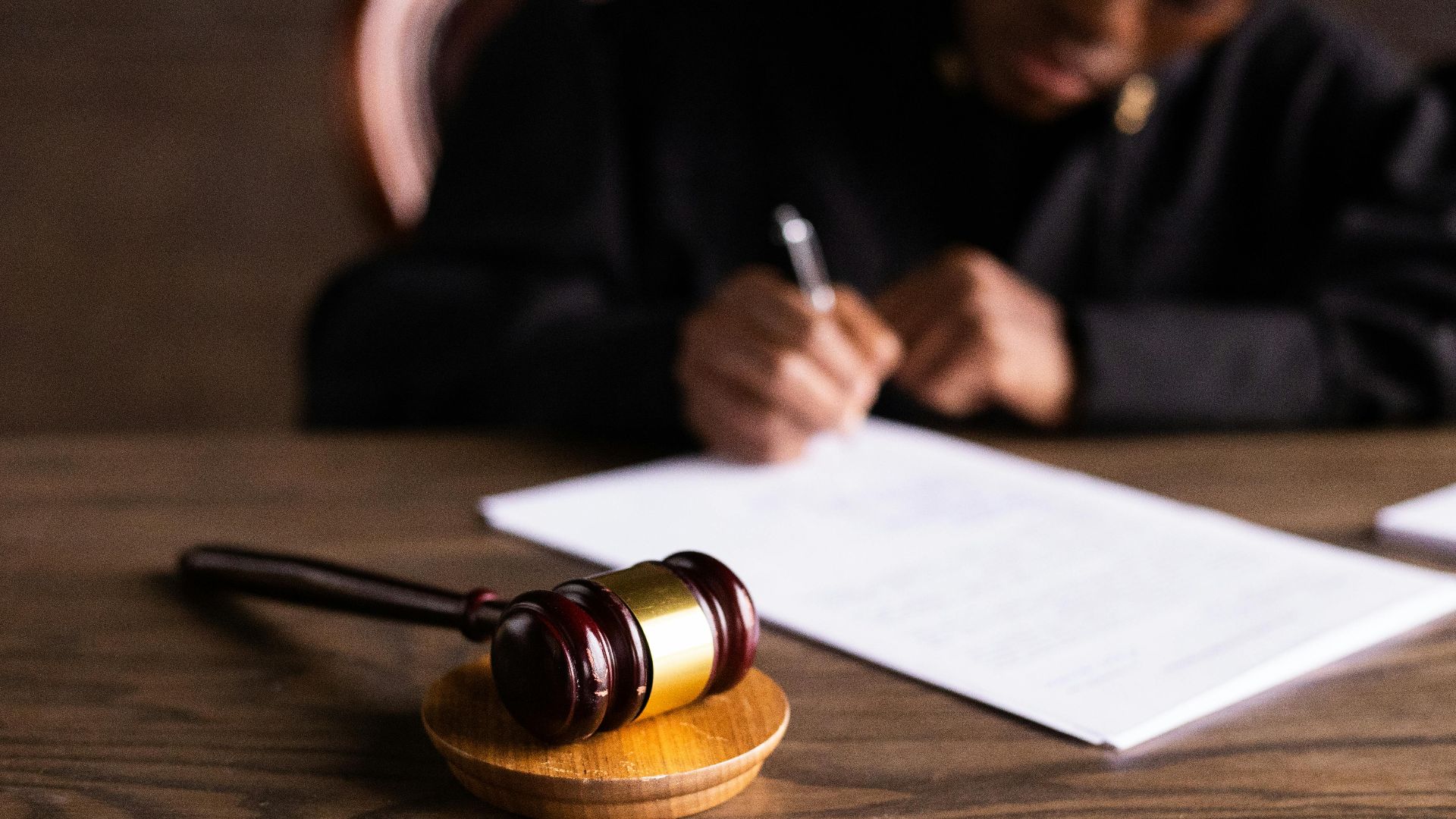 Judge signing documents at desk with focus on gavel, representing law and justice.