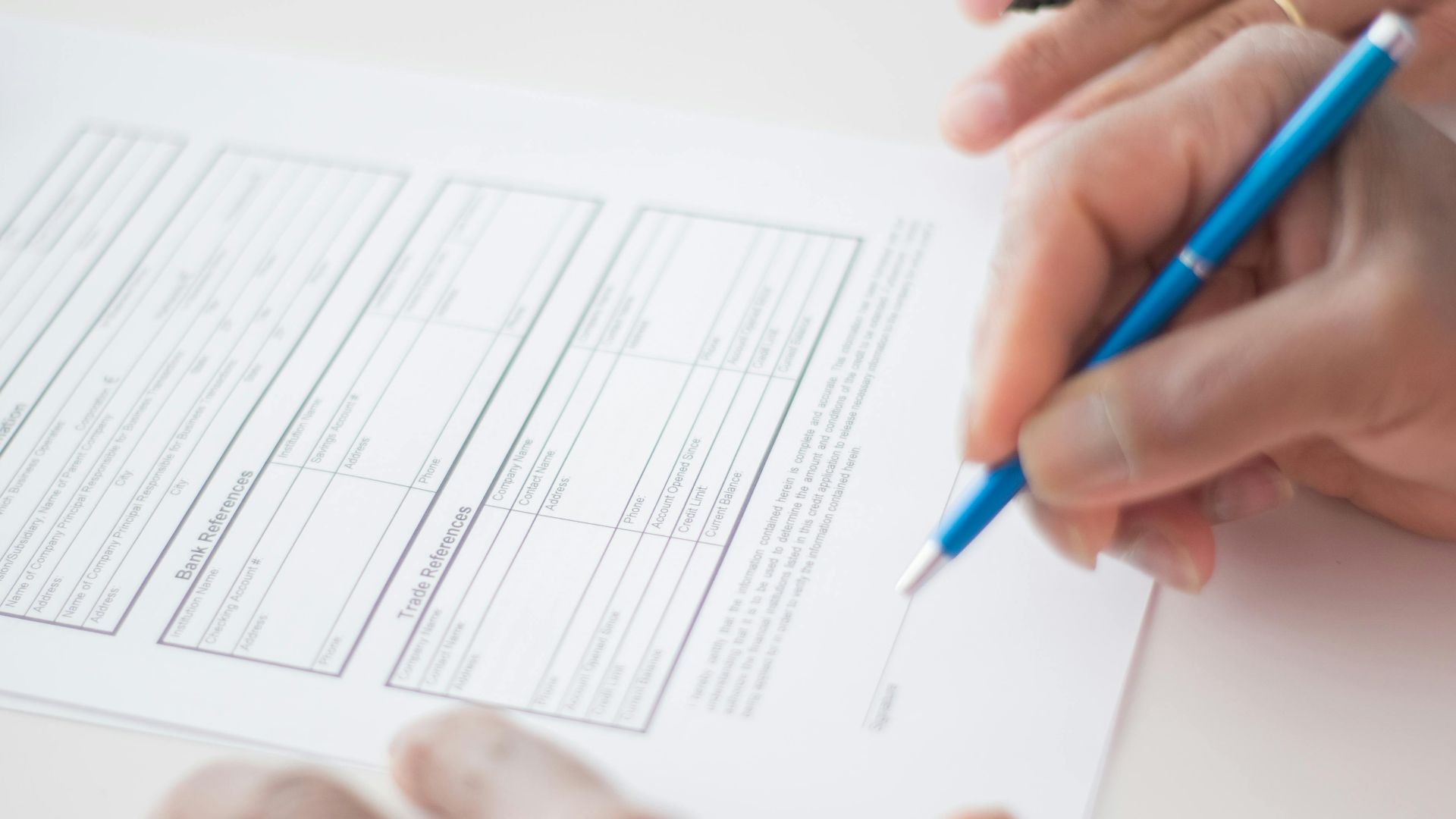 Close-up of hands signing a business document on a white surface with a pen.