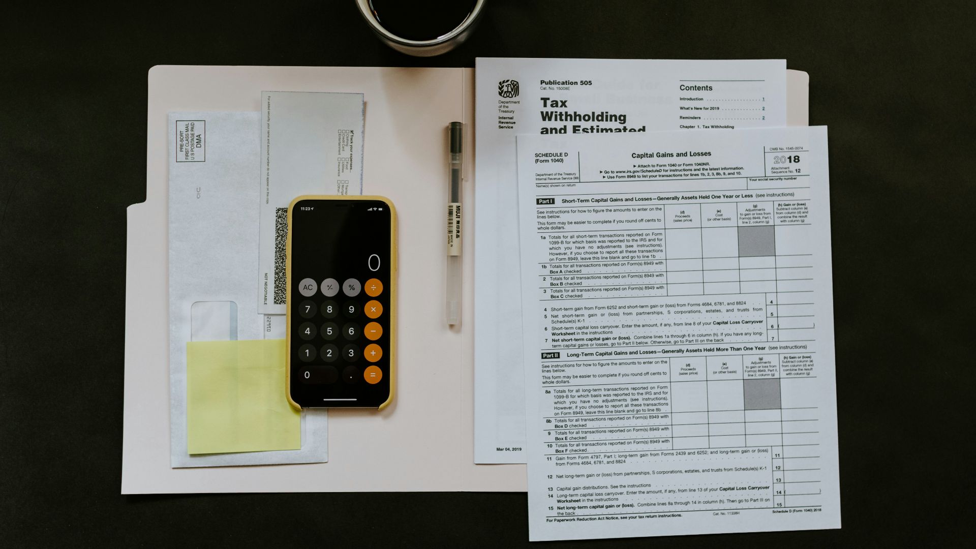 black Android smartphone near ballpoint pen, tax withholding certificate on top of white folder