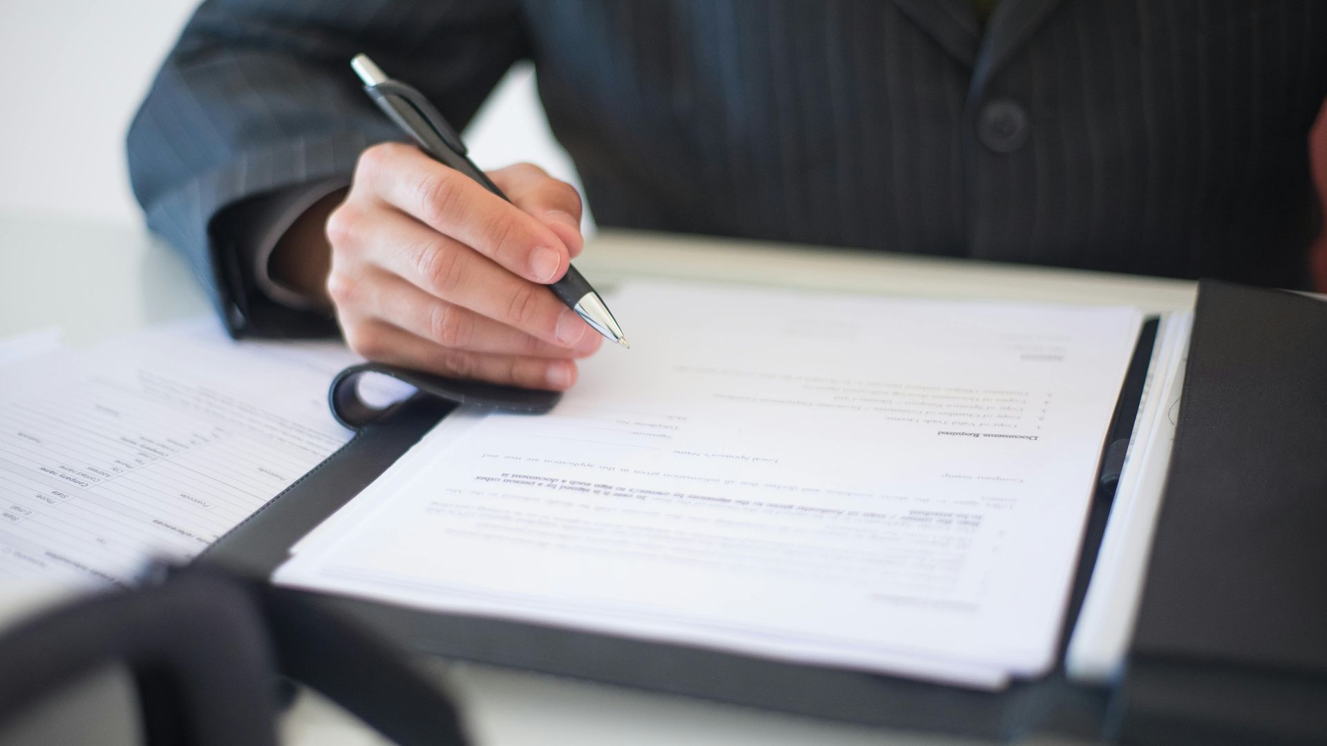 Close-up of a hand signing documents with a pen, symbolizing an important business contract.