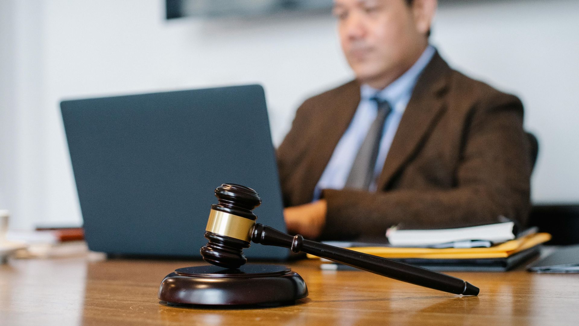Crop concentrated Asian male judge in formal clothes sitting using modern netbook while working in law office
