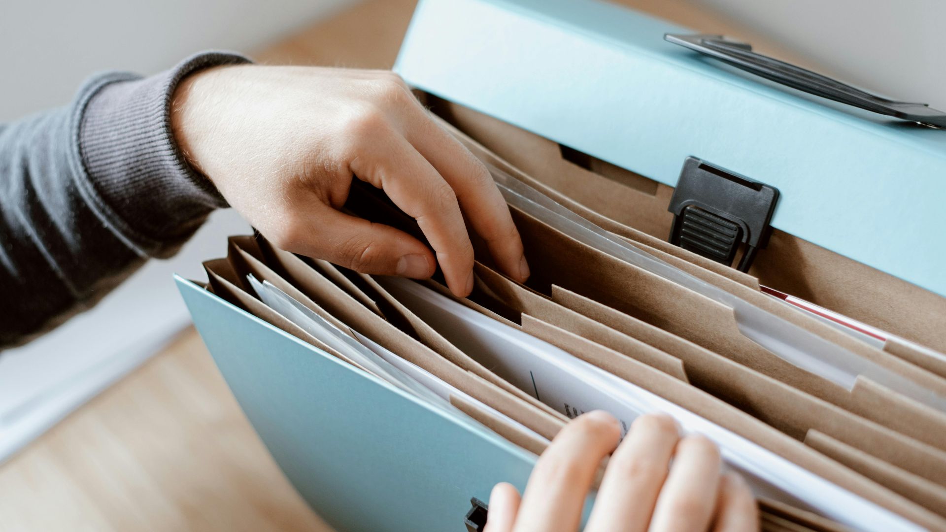 Crop unrecognizable person selecting document in opened briefcase for documents placed on wooden table