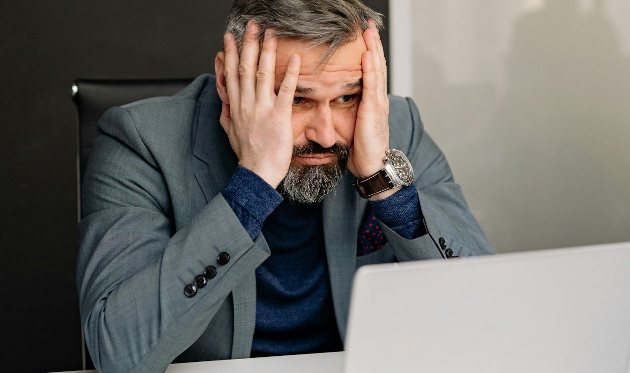 Man with His Hands on His Face While Looking at the Screen of a Laptop