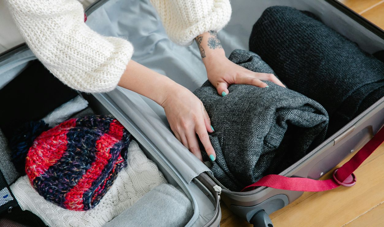 Person Putting Folded Clothes in Luggage