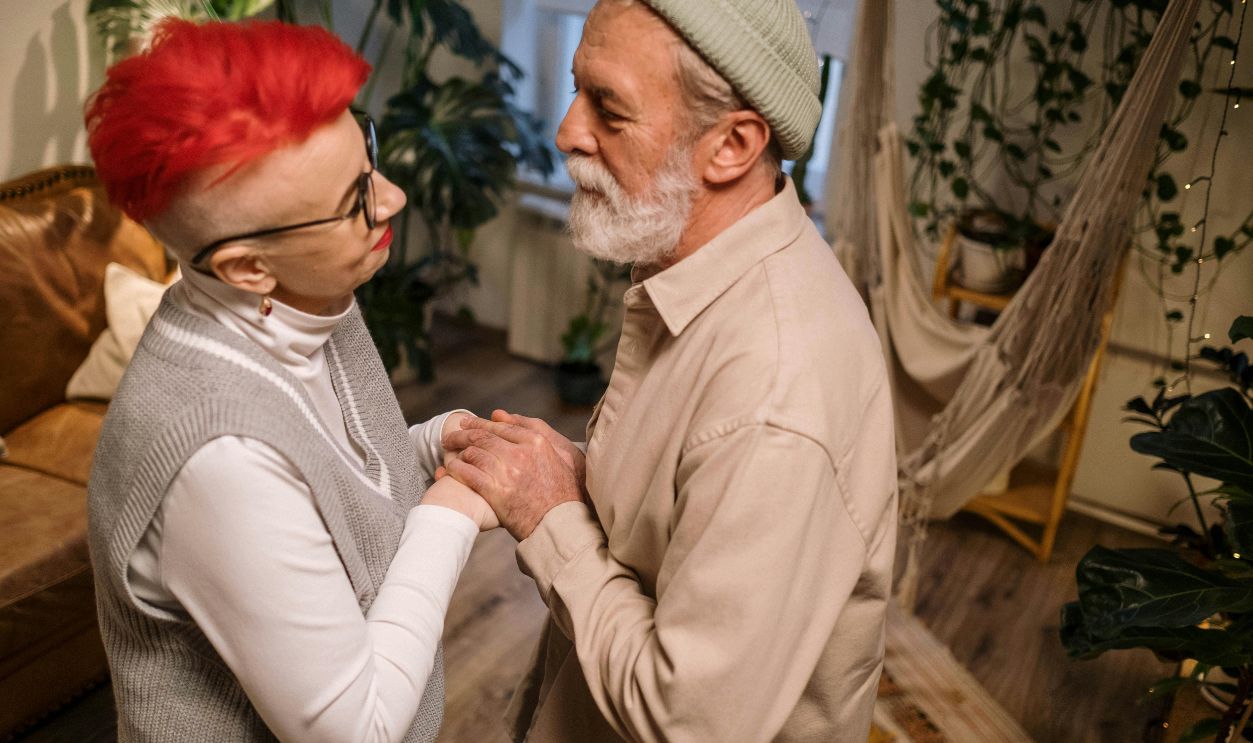 Photo of an Elderly Man Holding the Hands of an Elderly Woman with Red Hair