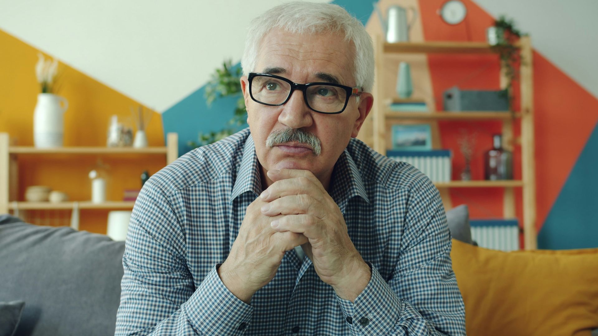 Elderly man with glasses resting chin on hands.