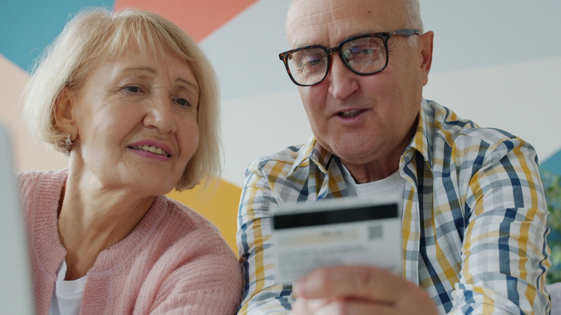 Elderly couple looking at credit card and laptop.