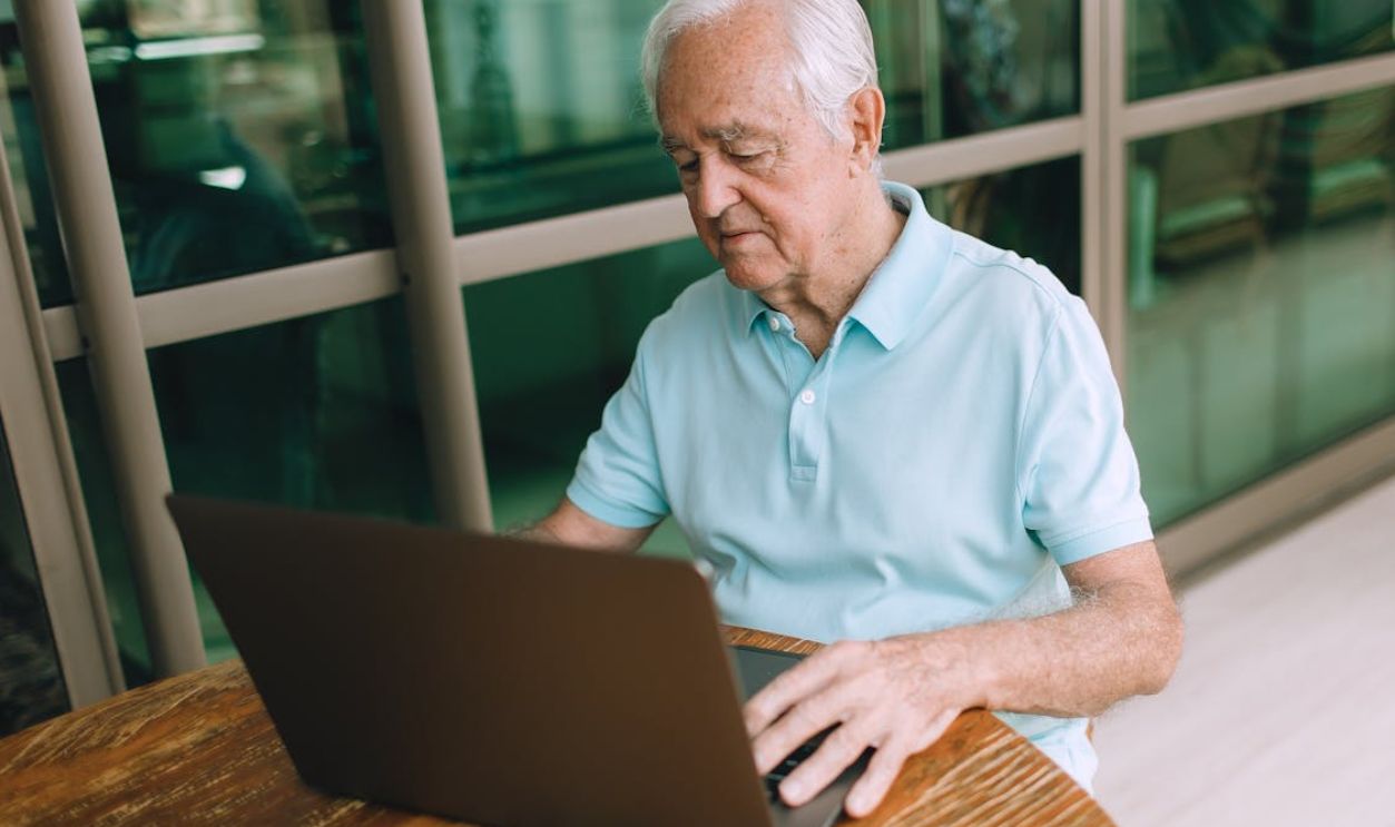 Sad Senior Man Sitting at Table with Laptop