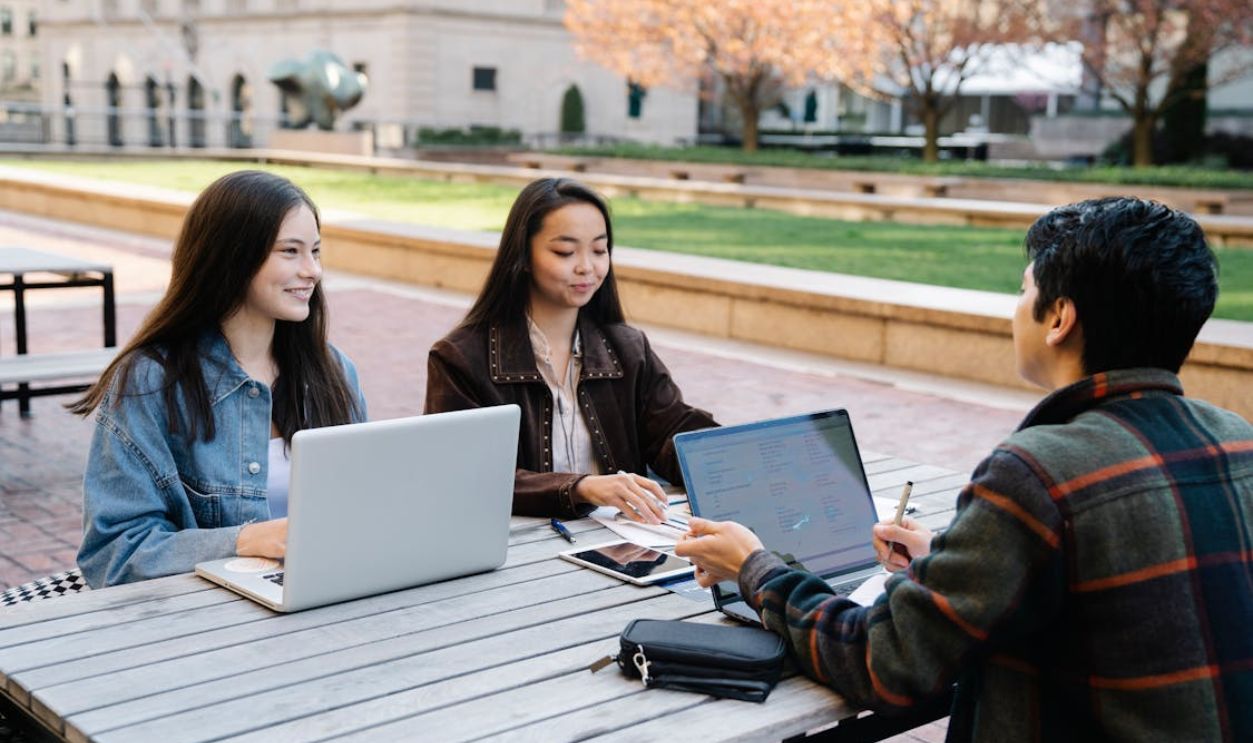 Three Young People Studying Together Outdoors With Laptops