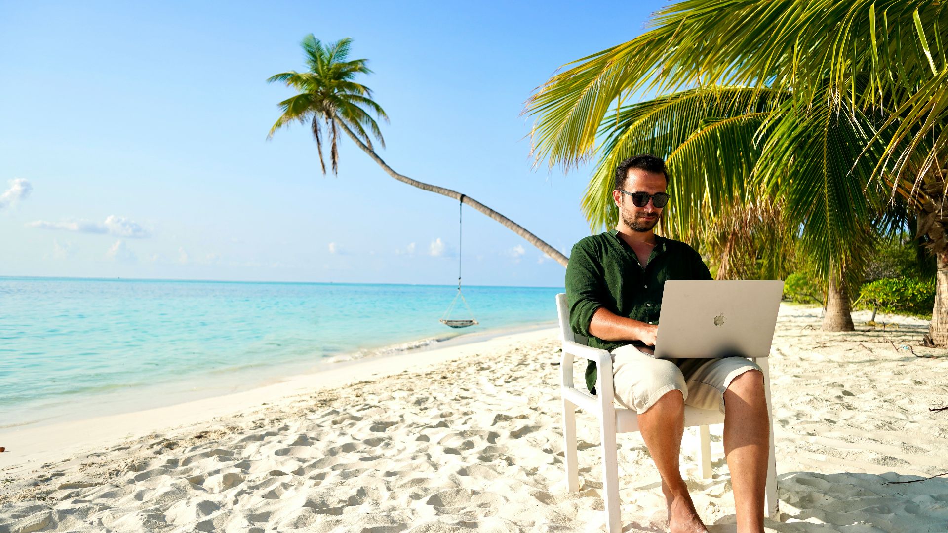 a man sitting in a chair on a beach using a laptop