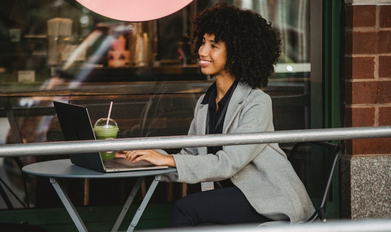 Smiling black freelancer typing on laptop on cafe terrace