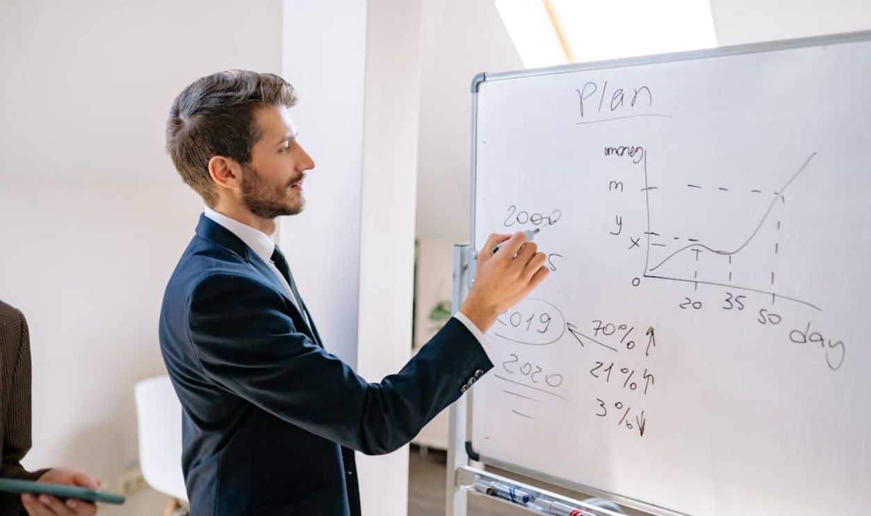 Man in Blue Suit Writing on White Board