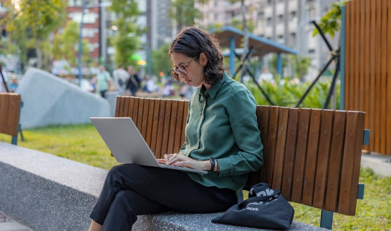 Young Woman Doing Concentrated Remote Work at Park Bench