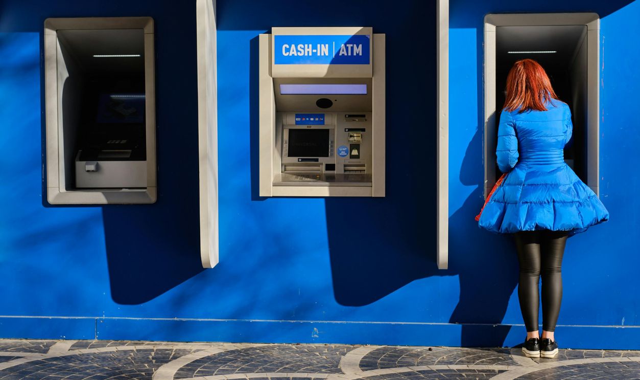Back View of a Woman in a Blue Dress Standing by the Wall with an ATM Machine