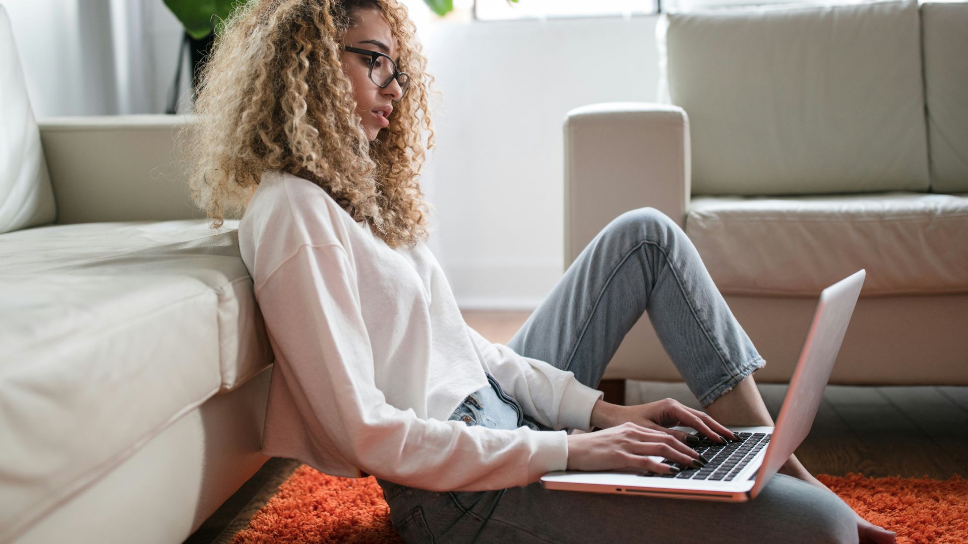 woman sitting on floor and leaning on couch using laptop