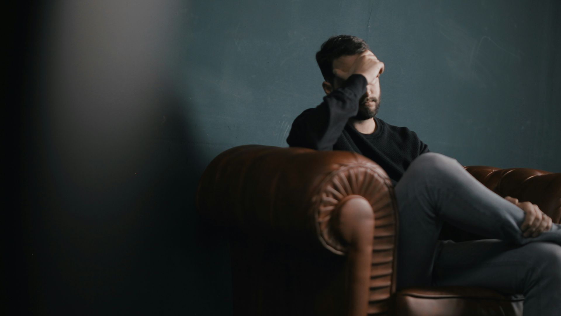 a man holds his head while sitting on a sofa