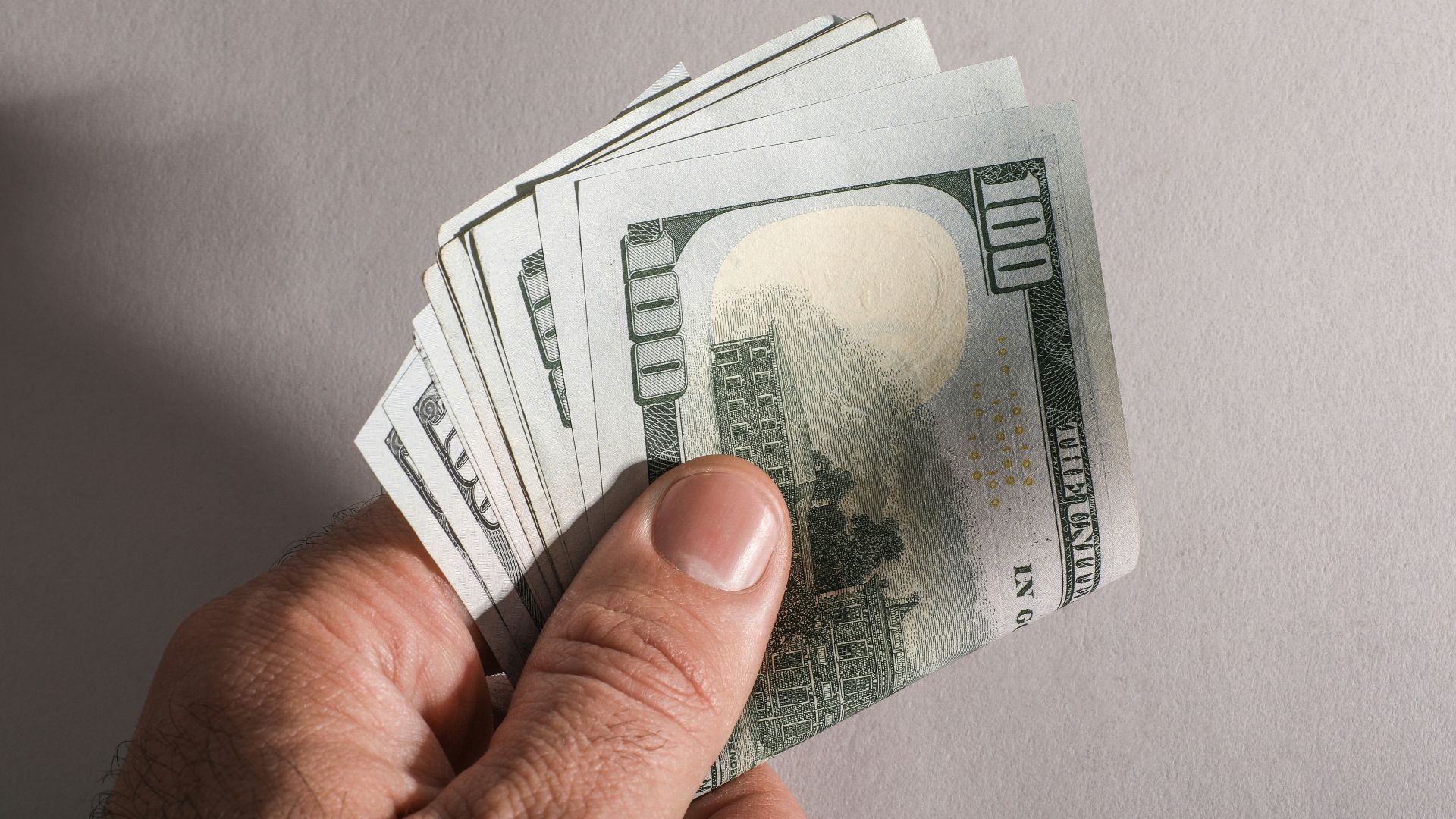 A hand holding a fan of us hundred dollar bills