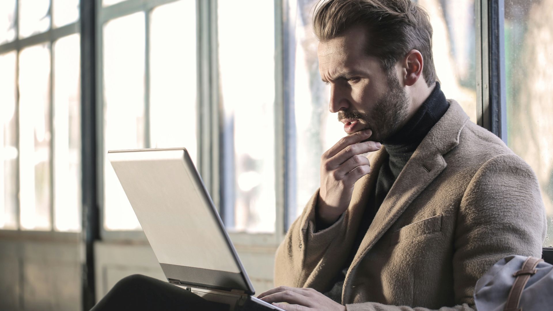 man holding his chin facing laptop computer