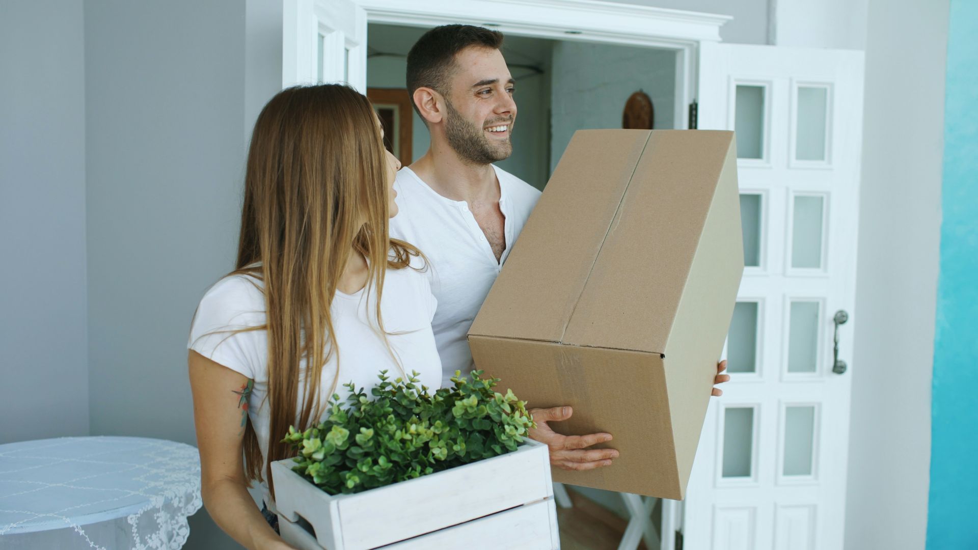 Couple carrying moving boxes into a new home