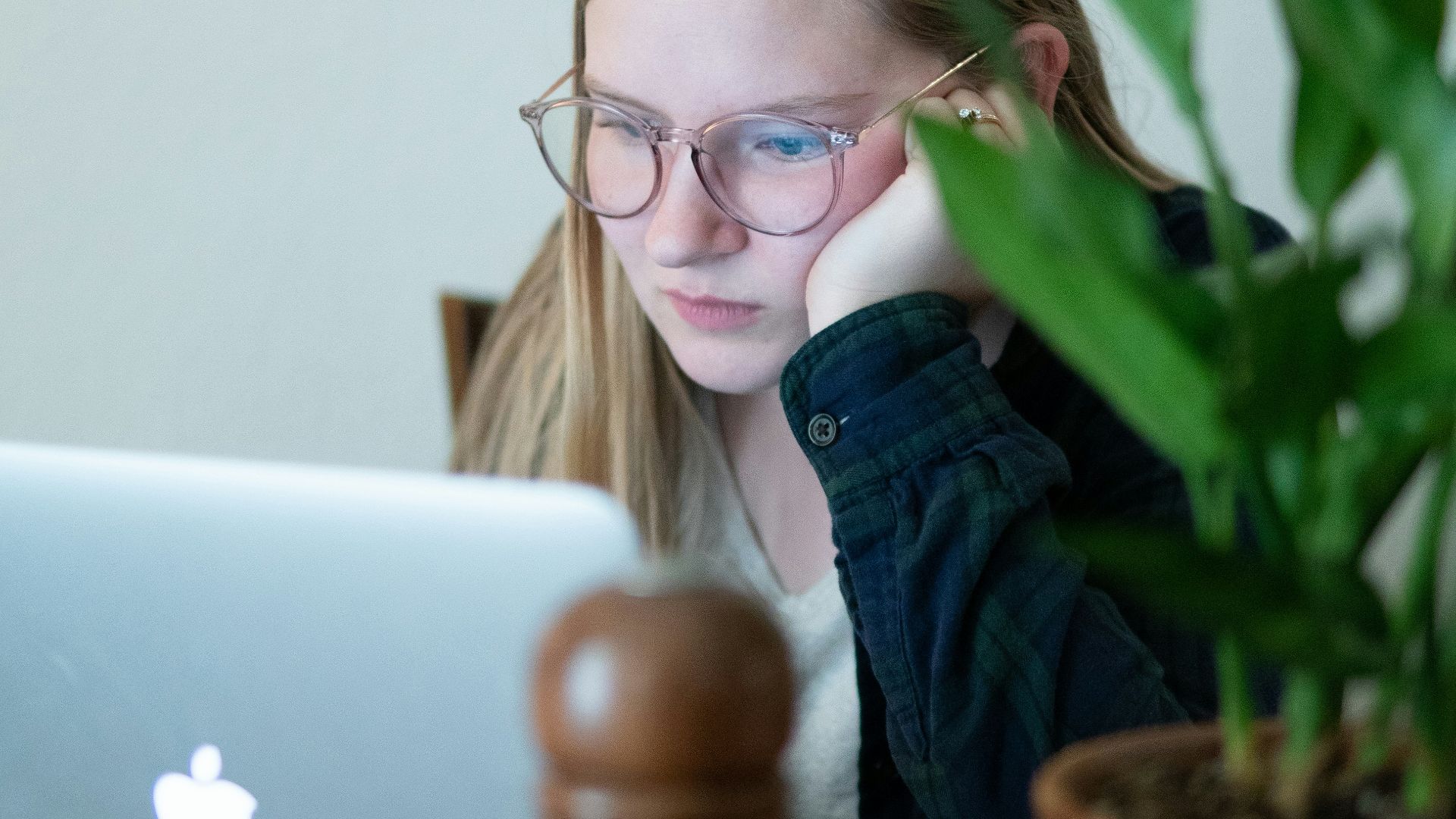 woman in blue denim jacket wearing eyeglasses sitting beside table with macbook
