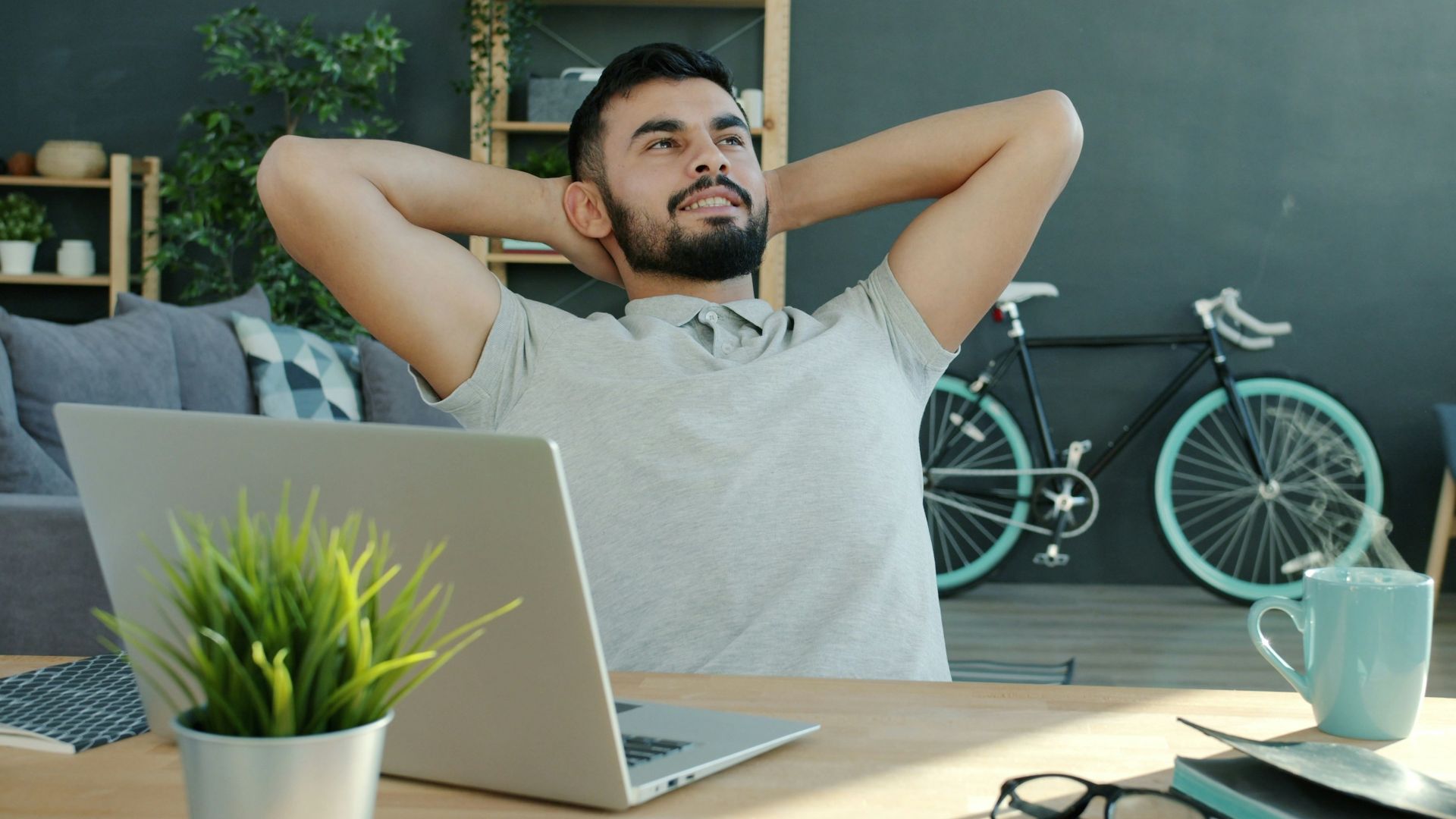 Man relaxing at desk with laptop and bicycle.