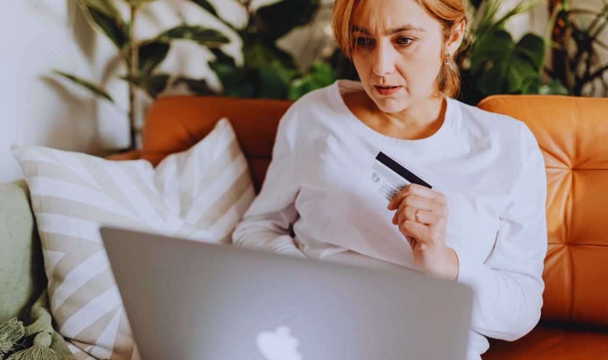 Woman Sitting on a Couch Using a Laptop and Holding a Credit Card