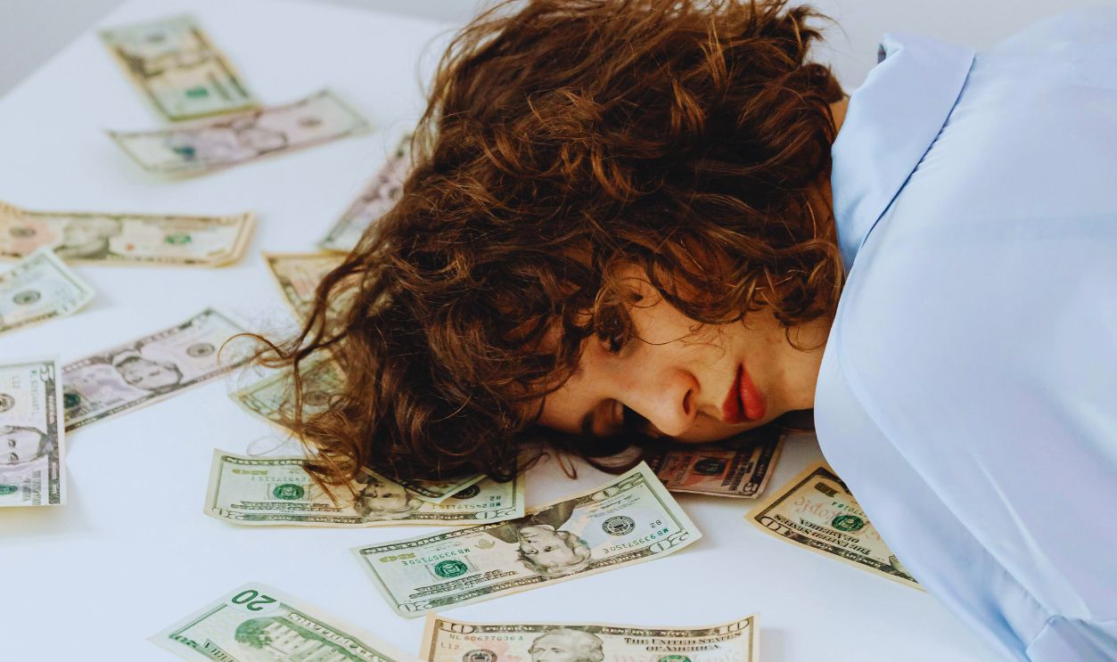 Curly-Haired Woman Lying Her Head on White Table with Paper Money