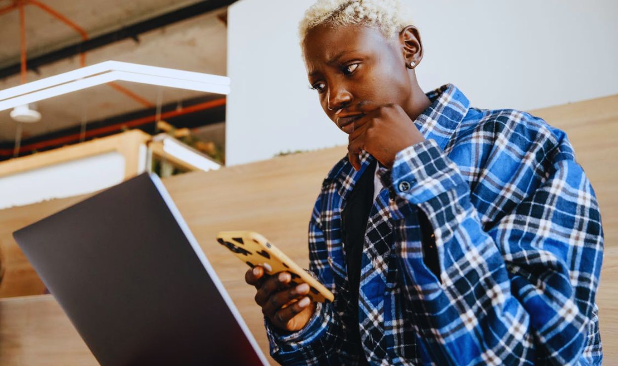 Thoughtful black woman using smartphone and laptop