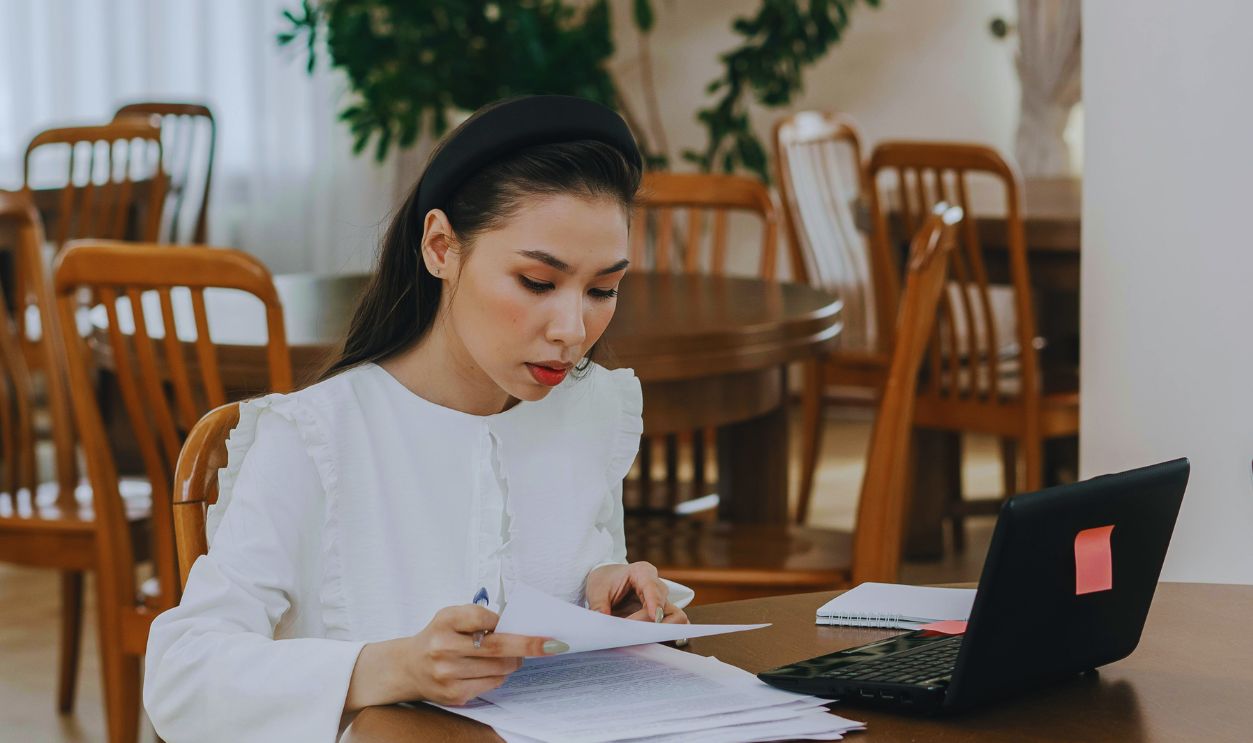 A Woman in White Dress Sitting on Wooden Chair while Studying