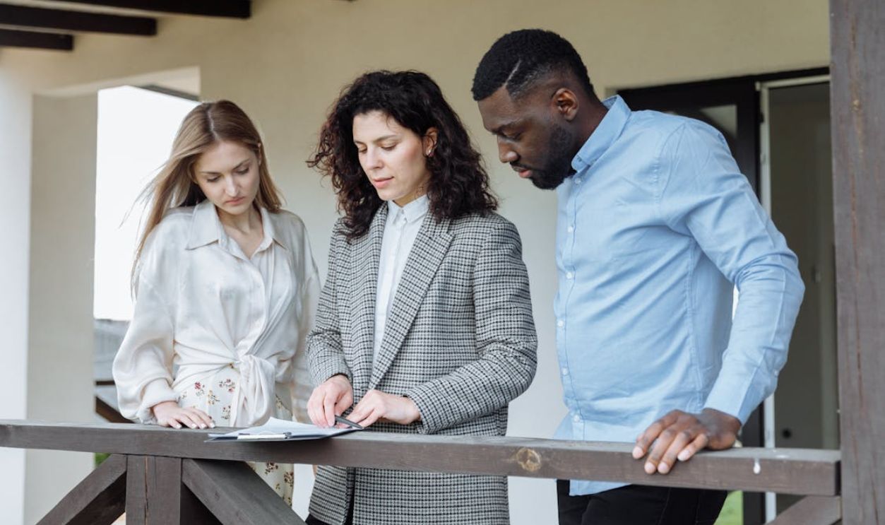 People Standing Near Wooden Railing while Looking at the Document on the Clipboard