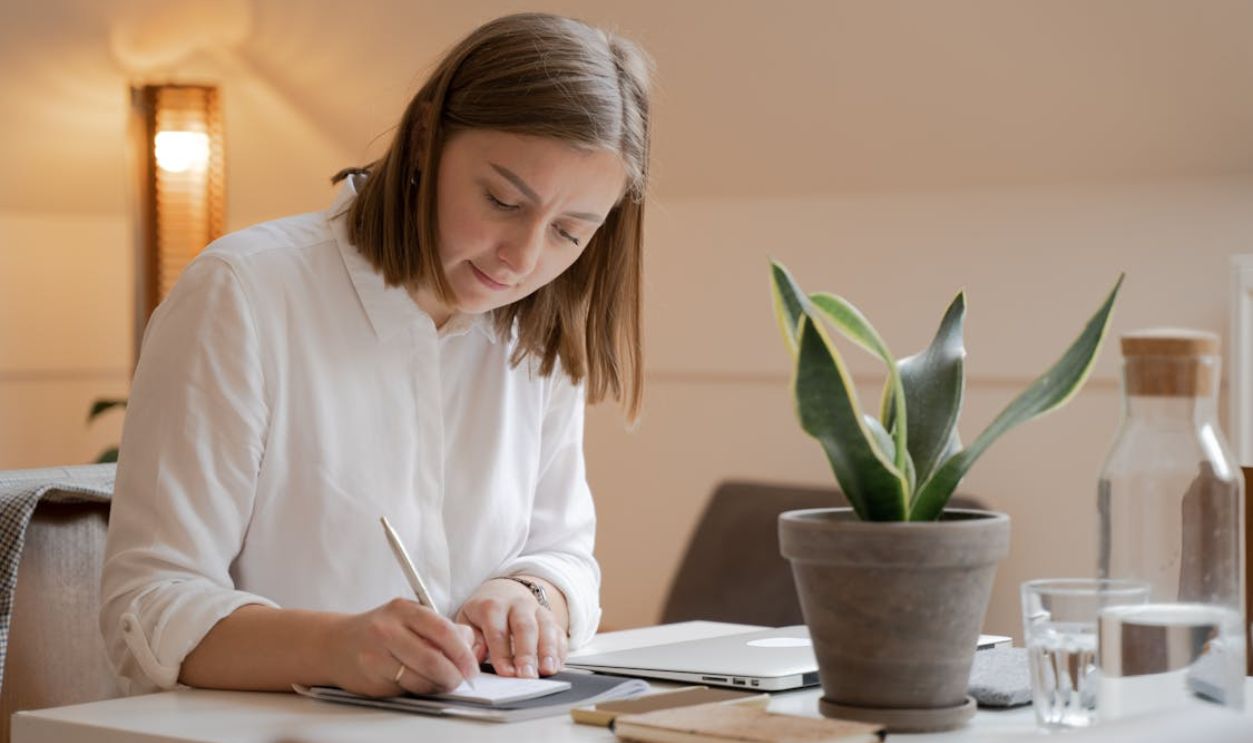A Woman in White Long Sleeves Writing on the Table
