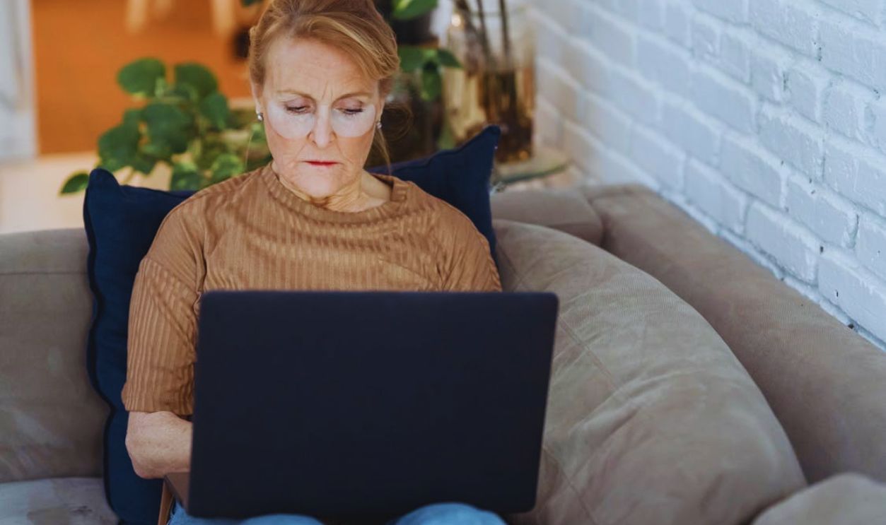Serious mature woman working on laptop on sofa