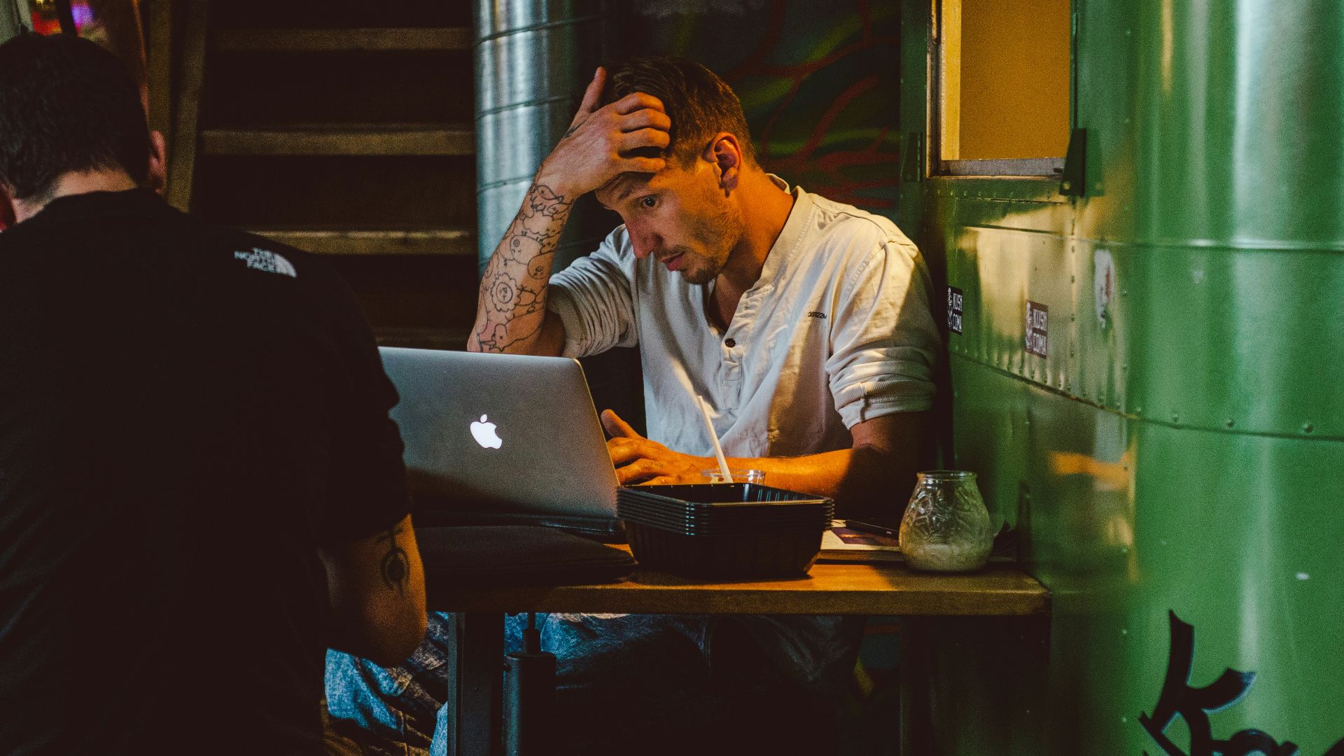 man in front of silver MacBook while scratching his head