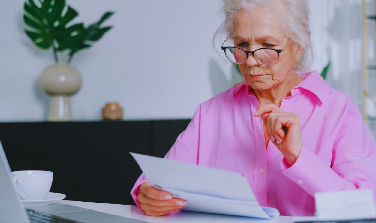 An Elderly Woman in Pink Long Sleeves Looking at Documents while Sitting