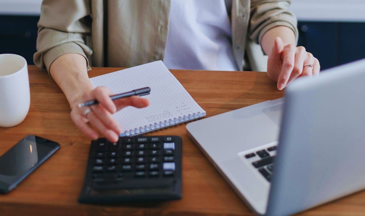Woman Using a Calculator While Sitting In Front of a Laptop